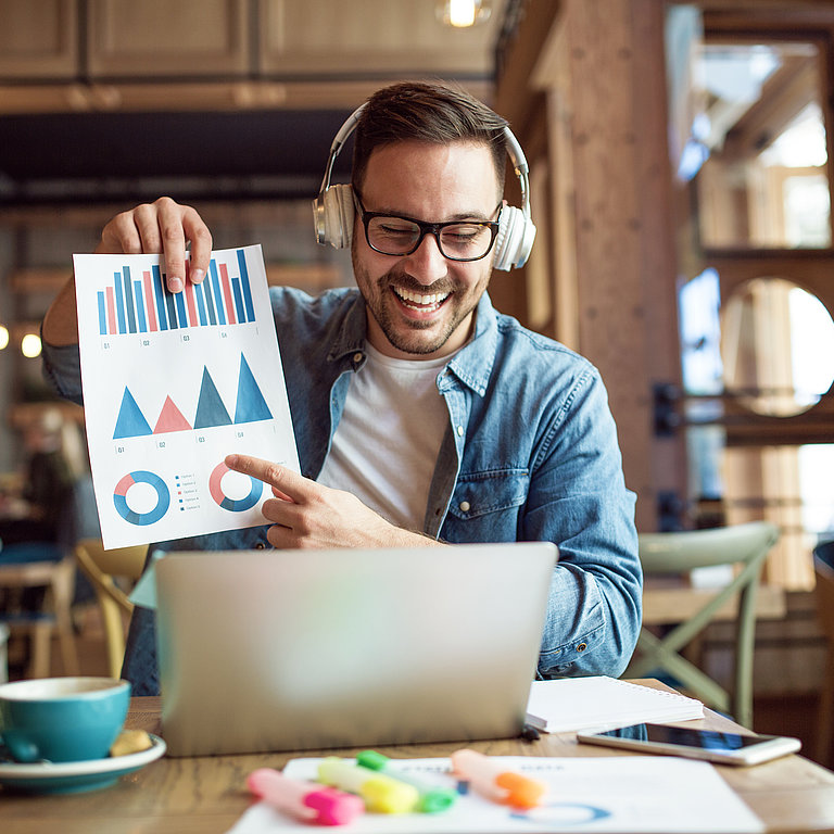 Become a Speaker Mann sitzt vor Laptop und hält Blatt mir Grafiken hoch